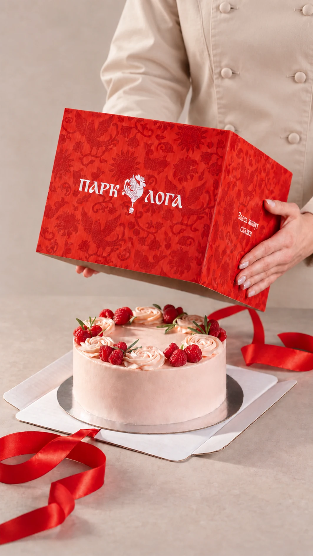 Открытая красная коробка с тортом, украшенным малиной и кремом